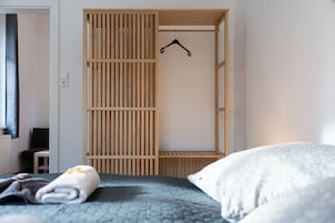 A bedroom with a bed, a wooden wardrobe, and a hanging rack.