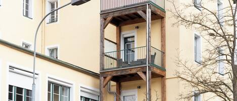 Un immeuble à plusieurs étages, doté d’un balcon au deuxième étage, d’un lampadaire et d’un arbre au premier plan.