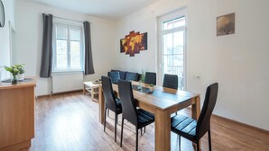 Una sala moderna con una mesa de comedor de madera, sillas negras, un sofá y un ventanal con cortinas.