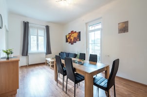 Una sala moderna con una mesa de comedor de madera, sillas negras, un sofá y un ventanal con cortinas.