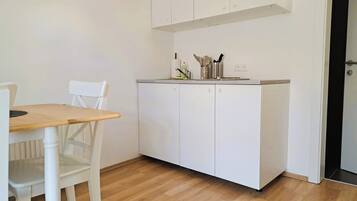 Une petite cuisine avec des meubles blancs, une table en bois et une chaise blanche.