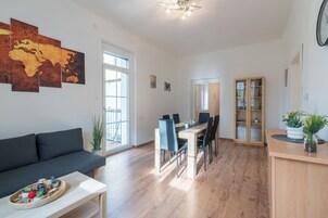 A modern living room with a dark sofa, a dining area with a wooden table and chairs, and a large world map on the wall.