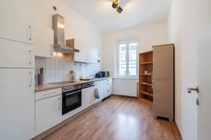 A modern kitchen with white cabinets, a built-in oven, and a window with blinds.