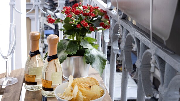 A balcony with a wooden table, two bottles of wine, a bowl of chips, and a potted plant with red flowers. - Sun&City Naples (Naples)