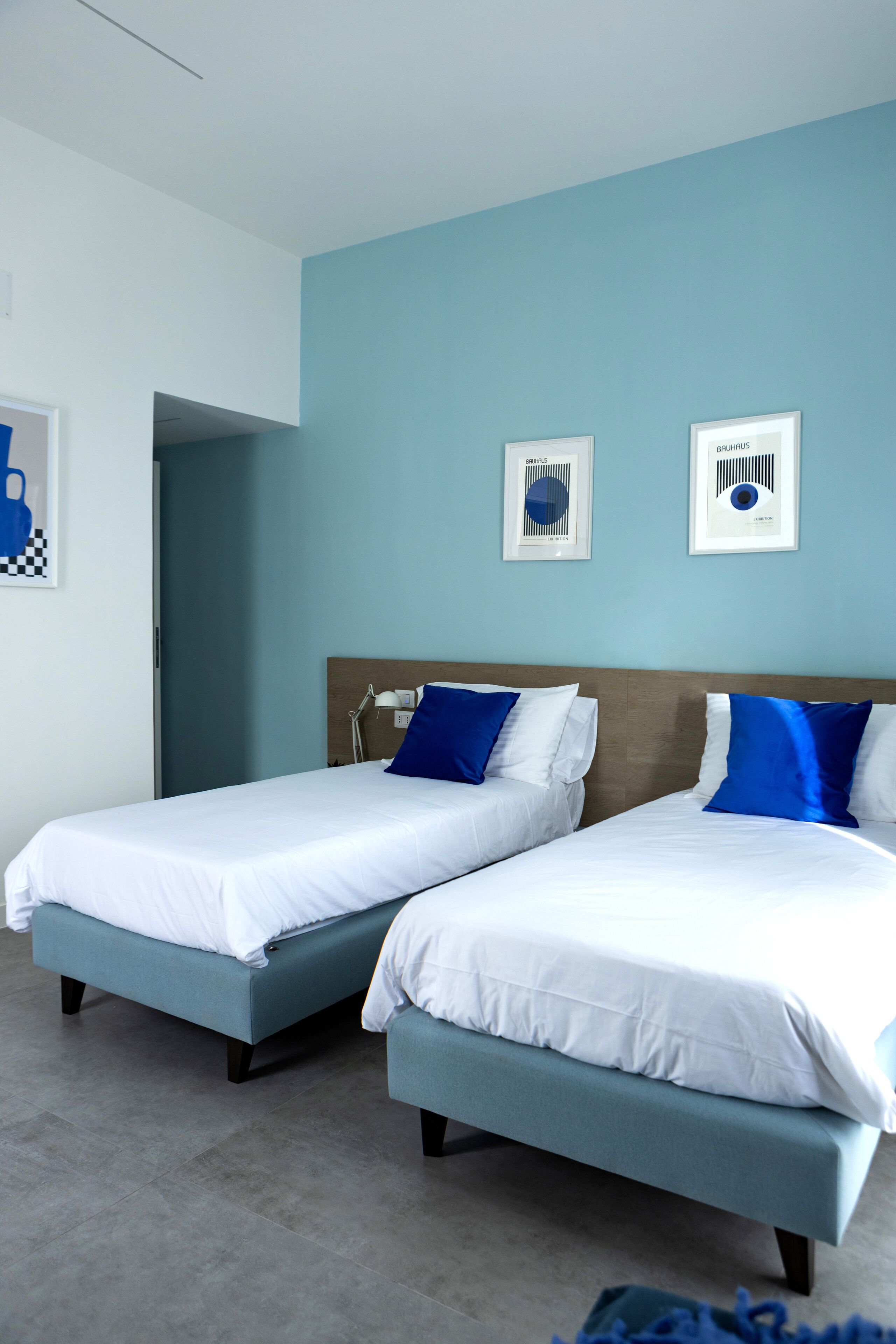Une chambre d’hôtel avec deux lits simples, une tête de lit en bois et un mur de couleur bleu clair.
