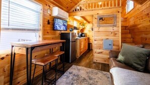 A cozy cabin interior with a wooden interior, a dining area with a bench, a kitchen with appliances, and a couch. - Couples Refuge by Ghosal Luxury Lodging (Sevierville)