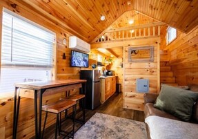 A cozy cabin interior with a wooden interior, a dining area with a bench, a kitchen with appliances, and a couch.