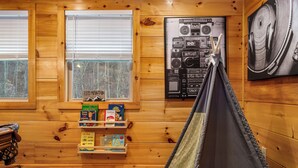 A cozy cabin interior with wooden walls, a bookshelf with children's books, a hammock, and a wall-mounted radio. - Couples Refuge by Ghosal Luxury Lodging (Sevierville)