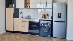 A modern kitchen with a built-in oven, microwave, and washing machine, featuring a herringbone wood floor and white cabinetry. - on Park by Smart City Stays (Cape Town)