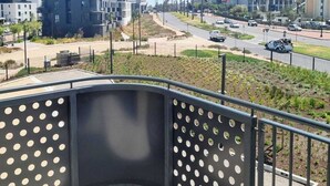 A balcony with a metal railing and perforated panels, overlooking a street with modern buildings and a clear sky. - on Park by Smart City Stays (Cape Town)
