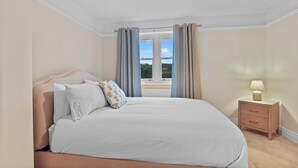 Un dormitorio con una cama grande, una mesita de noche con lámpara y una ventana con cortinas.