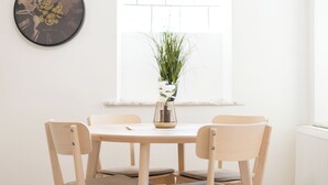 A dining area with a round table, four chairs, a world map clock, and a window with blinds. - revLIVING Apartments Gars am Kamp (Gars am Kamp)