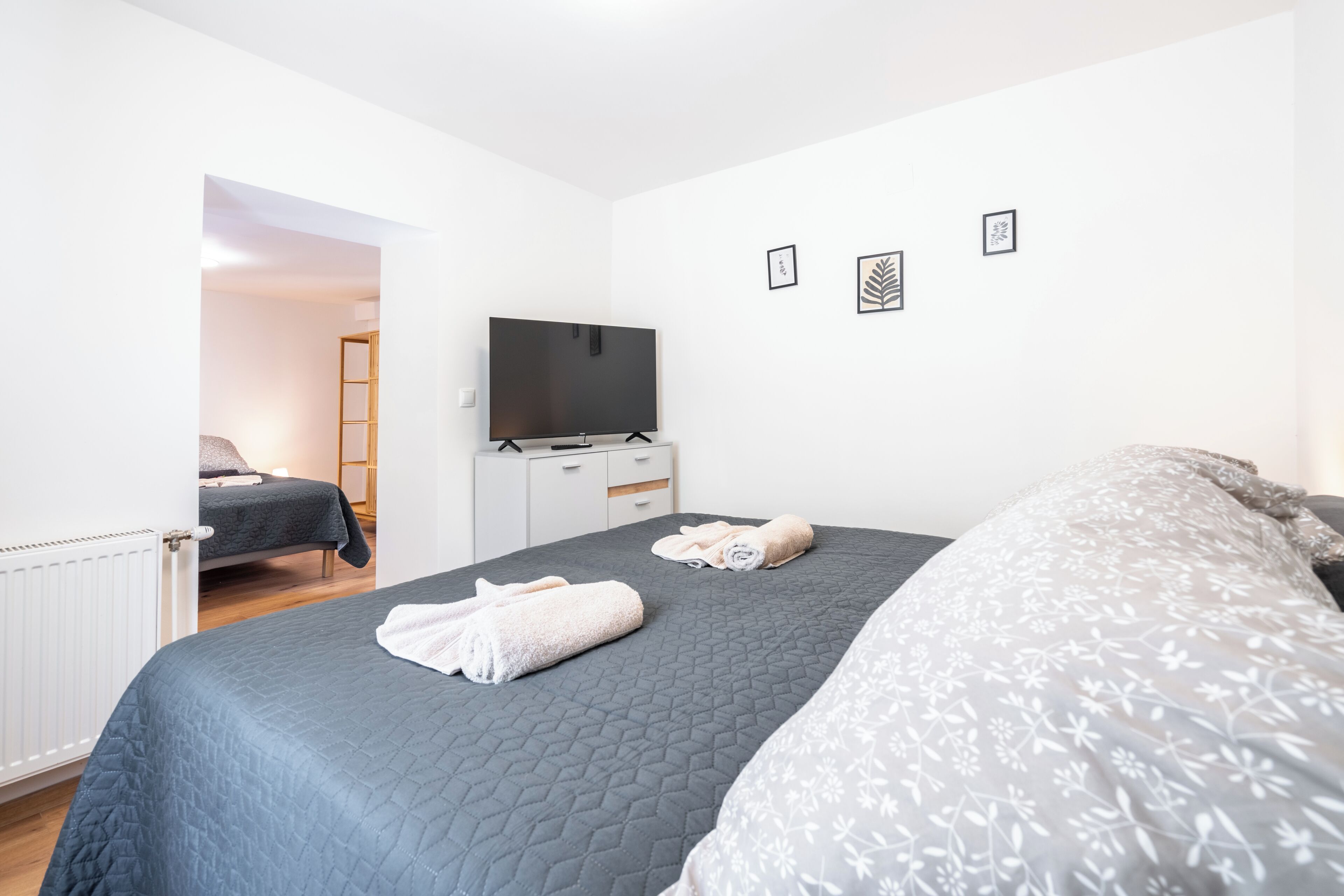 Un dormitori amb un llit, una televisió, un calaix i una porta que dona a una altra habitació.