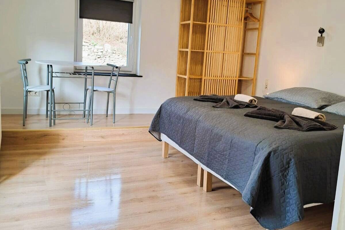 A bedroom with a bed, a desk with chairs, a window, and a wooden wardrobe.