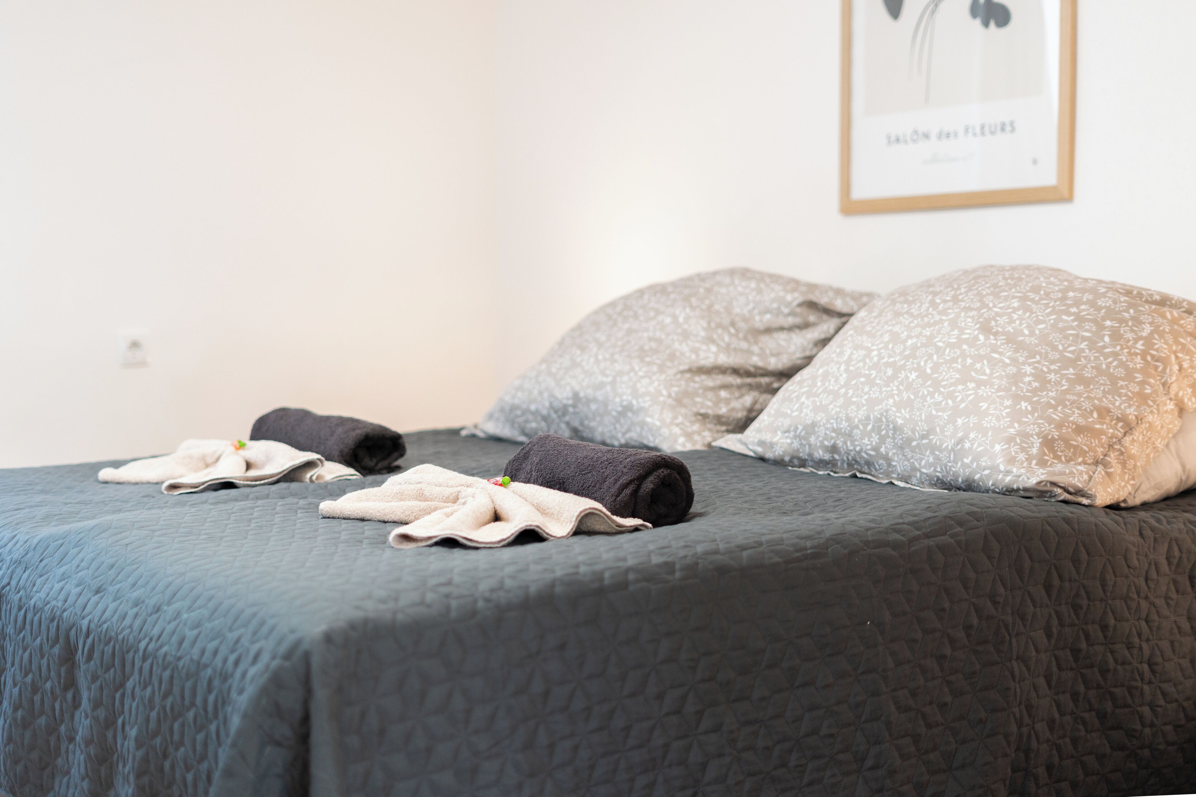 A neatly made bed with a dark quilt, two pillows, and three towels.