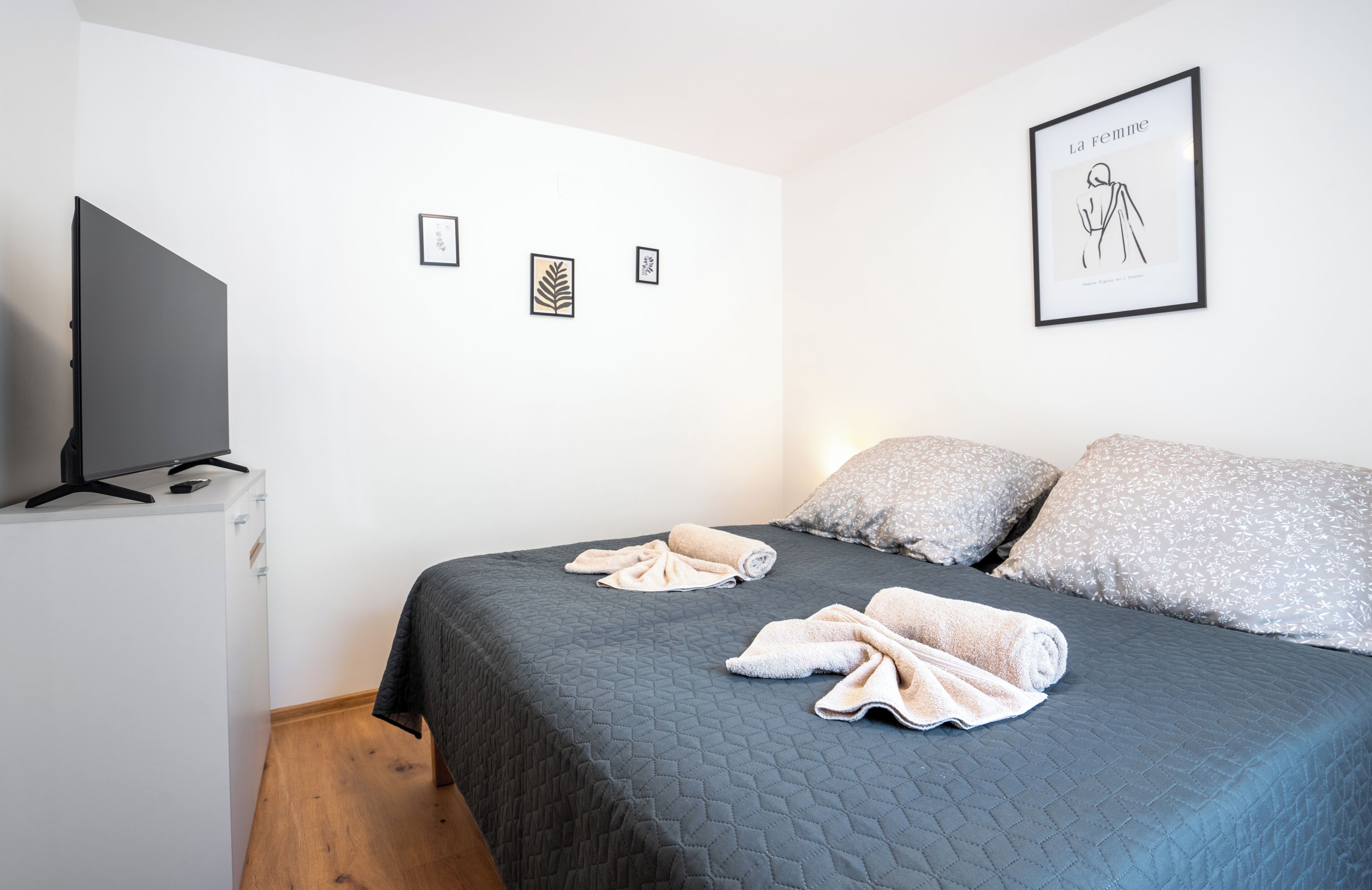 Un dormitorio con cama, almohadas, televisor y cuadros en la pared.