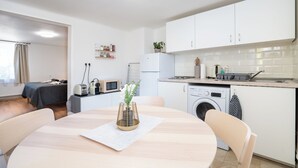 A modern kitchen with white cabinets, a built-in washing machine, and a dining area with a round table and chairs. - revLIVING Apartments Gars am Kamp (Gars am Kamp)