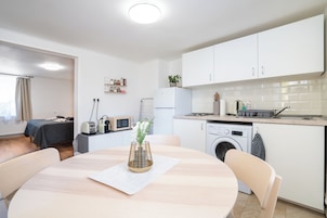 Una cocina moderna con armarios blancos, lavadora integrada y comedor con mesa y sillas redondas.