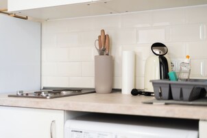 A kitchen with a white tiled backsplash, a stainless steel range hood, a kettle, and a coffee maker.