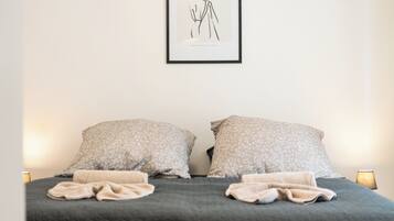 A neatly made bed with two pillows and a blanket, a framed artwork on the wall, and a bedside lamp.