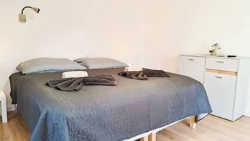 Una cama bien hecha con un edredón gris acolchado, dos almohadas estampadas y una lámpara de noche.