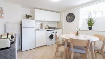 Een kleine keuken met een wasmachine, een eettafel met stoelen en een raam met een plant.