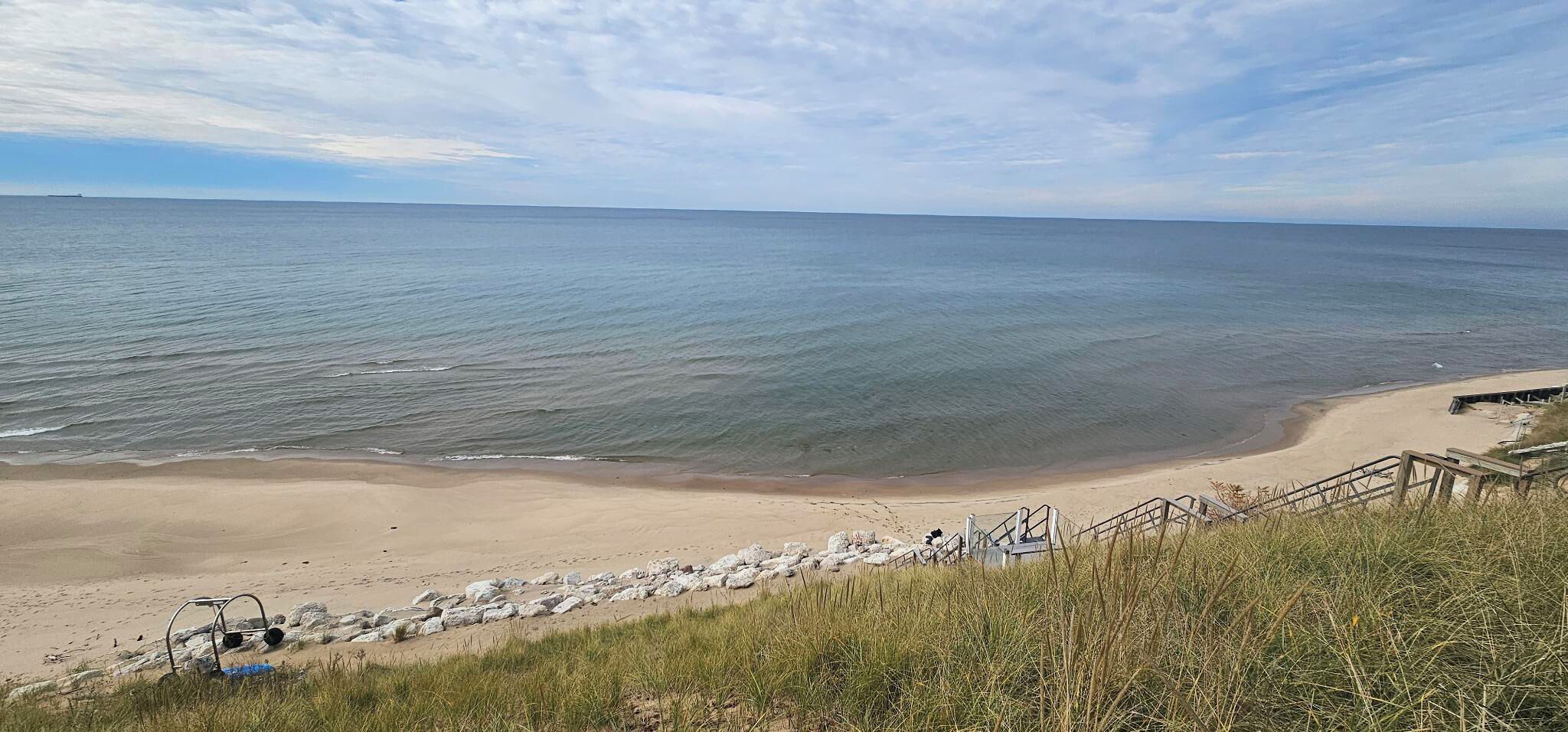 A beach with a wooden staircase leading down to the shore, surrounded by grass and rocks.