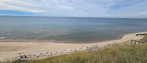 A beach with a wooden staircase leading down to the shore, surrounded by grass and rocks.