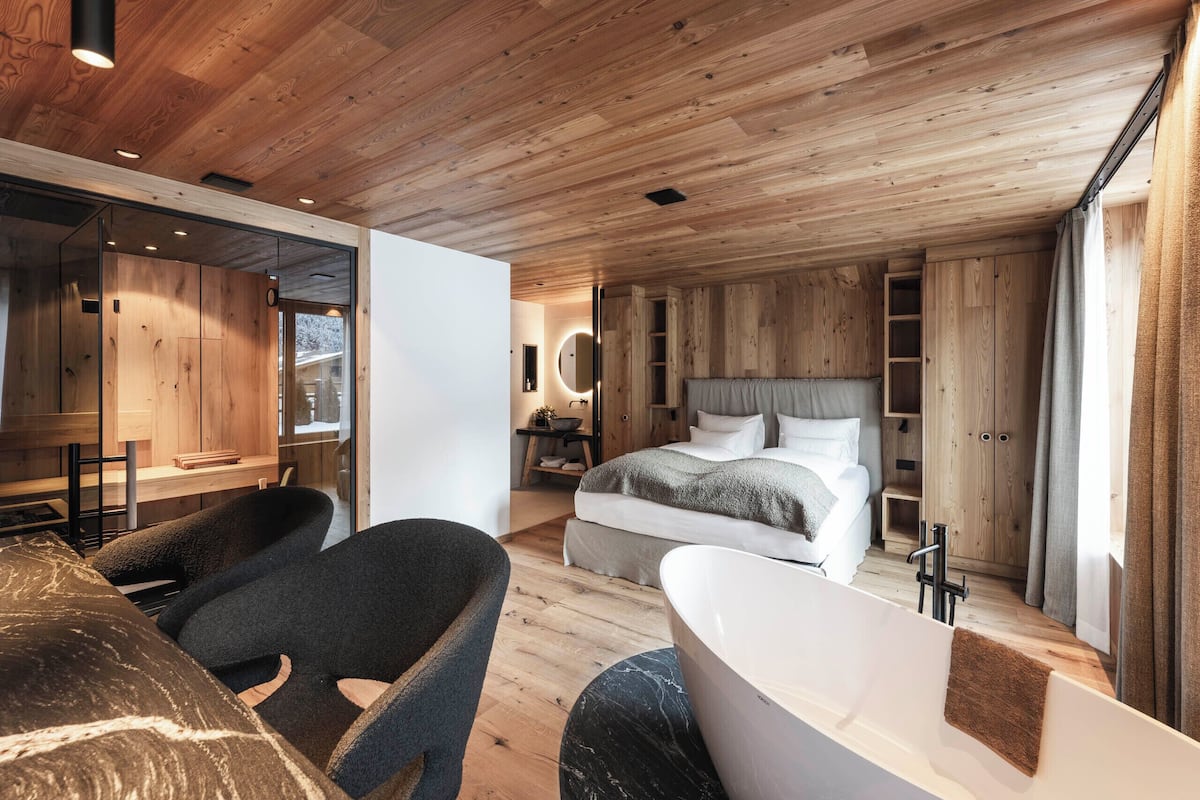 Une chambre moderne avec un grand lit, un coin salon avec un fauteuil, une baignoire et un lambris en bois sur les murs et le plafond.