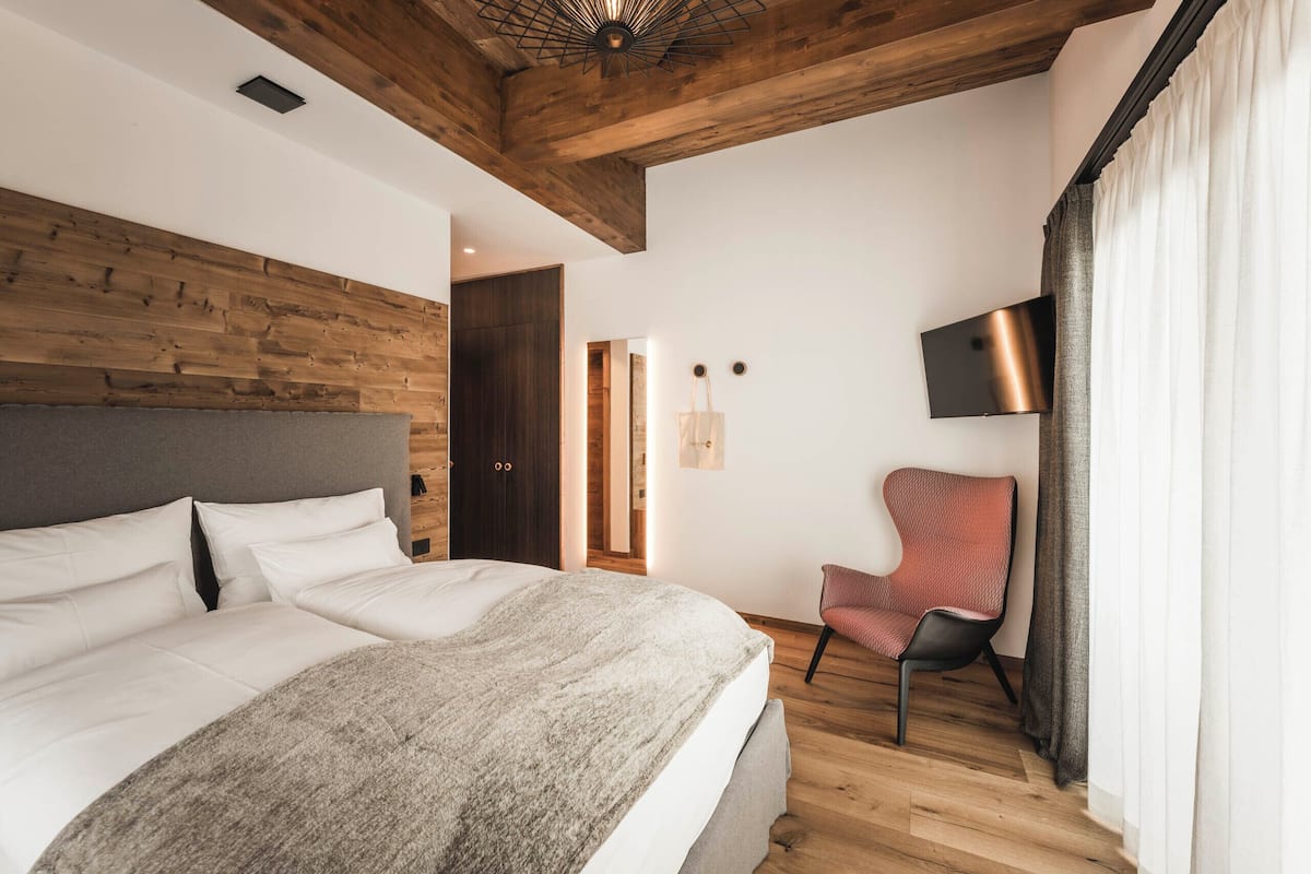 Une chambre moderne avec un plafond en bois, un grand lit, une chaise et un téléviseur fixé au mur.