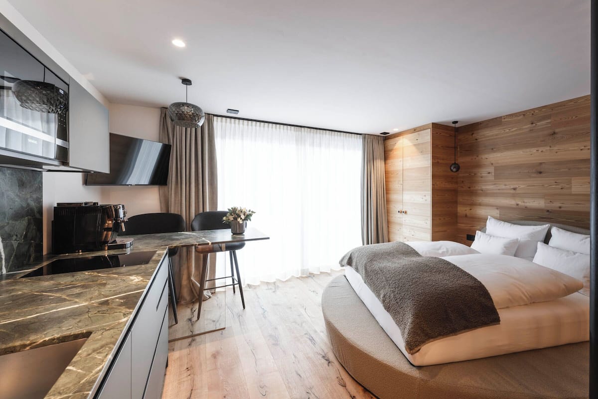 Une chambre d’hôtel moderne avec un mur d’accent en bois, un lit avec du linge de maison blanc, une machine à café et un téléviseur fixé au mur.