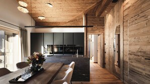 A modern interior with a wooden ceiling, a long dining table with chairs, and a kitchen in the background. - DISTINCTIVE LUXURY DOLOMITI APARTMENTS TERRE71 (Marebbe)