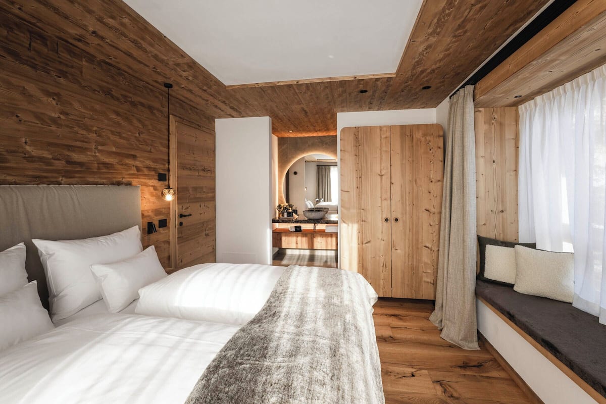 Une chambre avec un grand lit, des murs en bois, une banquette intégrée avec des coussins et une vue sur la salle de bain.