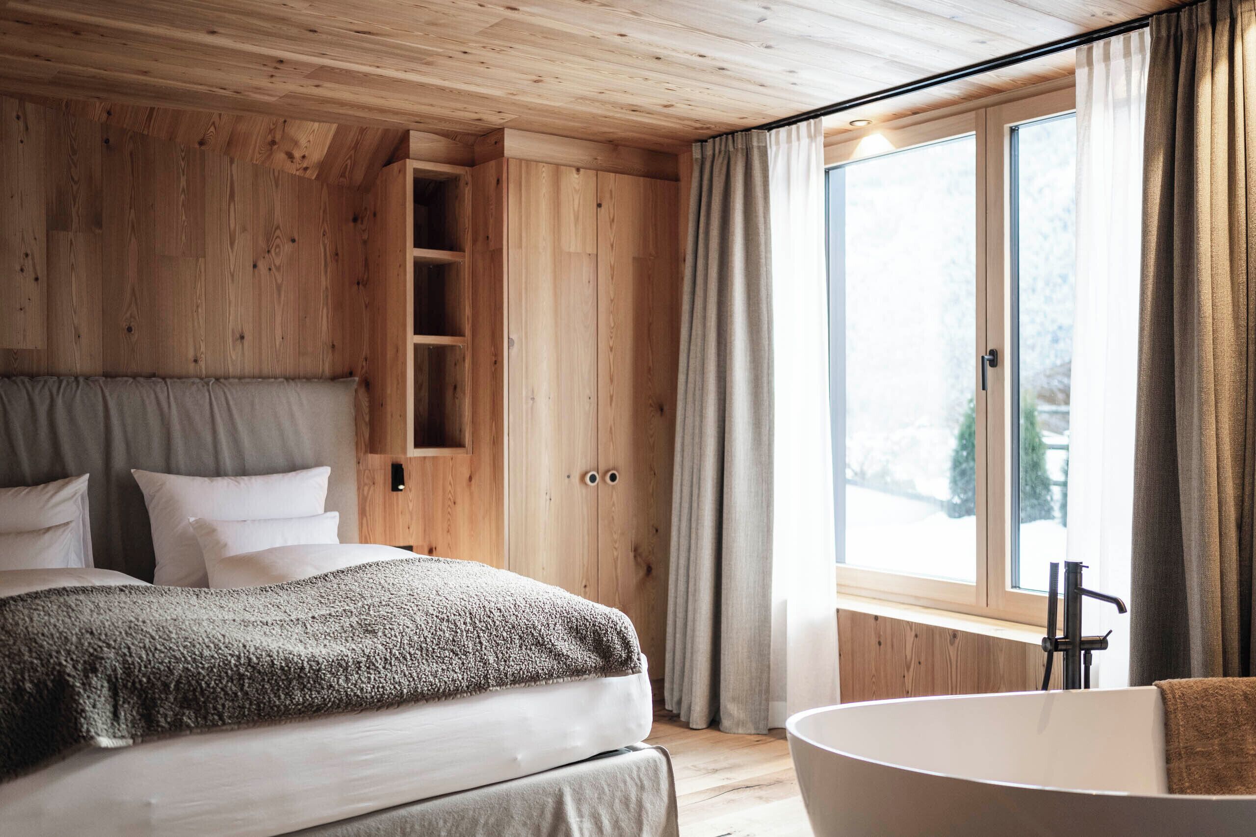 Un dormitorio con paneles de madera, un ventanal grande, una estantería empotrada y una bañera independiente.