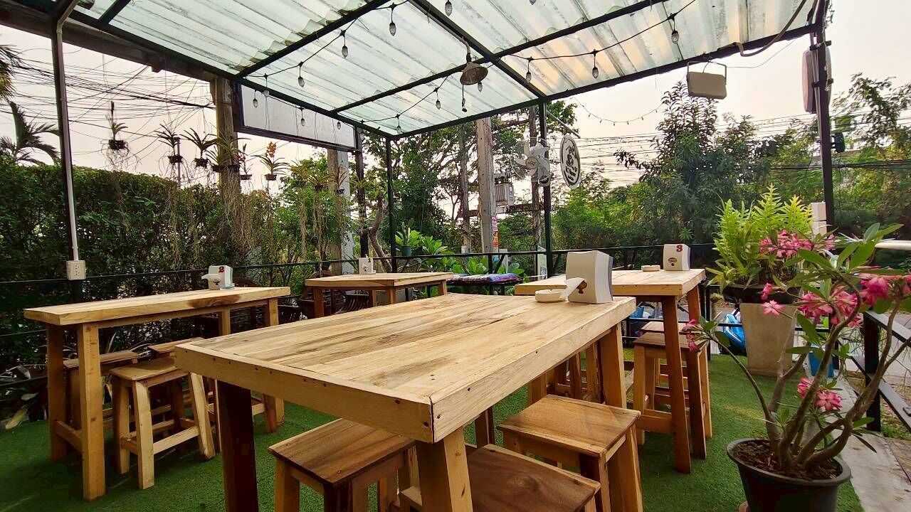 Una veranda esterna con tavoli e sedie in legno, immersa nel verde e circondata da piante in vaso.
