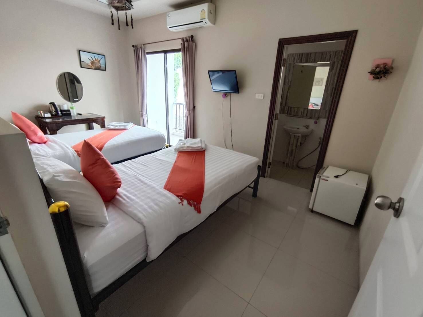 A hotel room with two beds, a TV, a small desk, a mirror, and a bathroom visible through an open door.