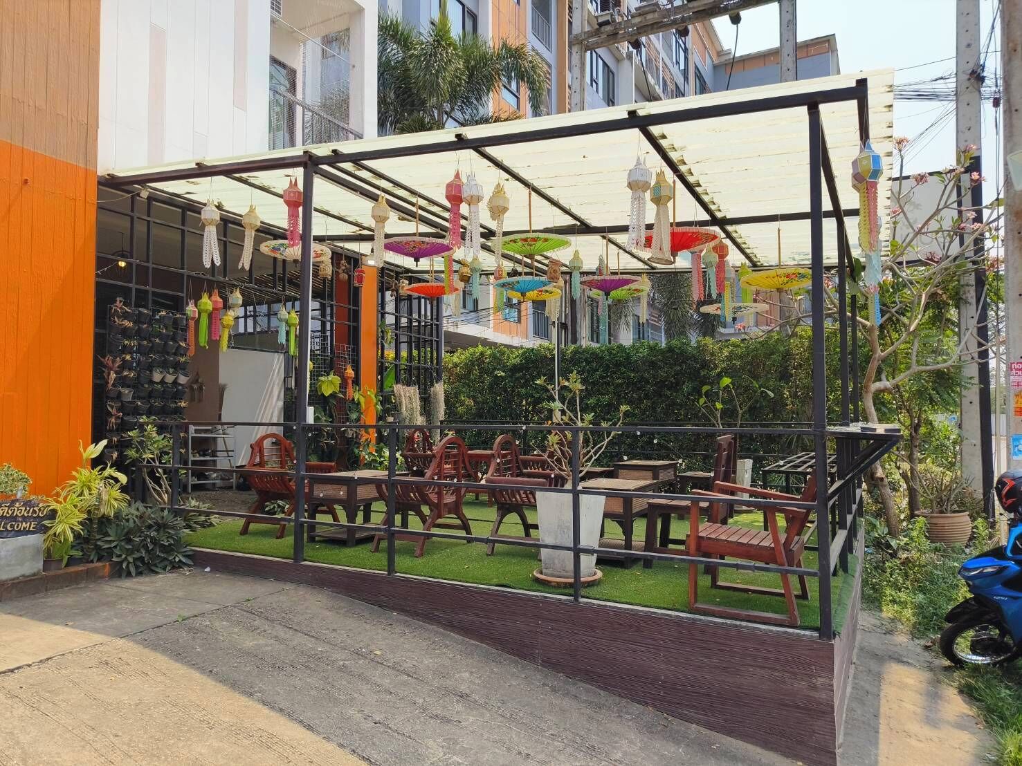 Un espace extérieur aménagé avec des tables et des chaises, entouré de plantes en pot et décoré de guirlandes.