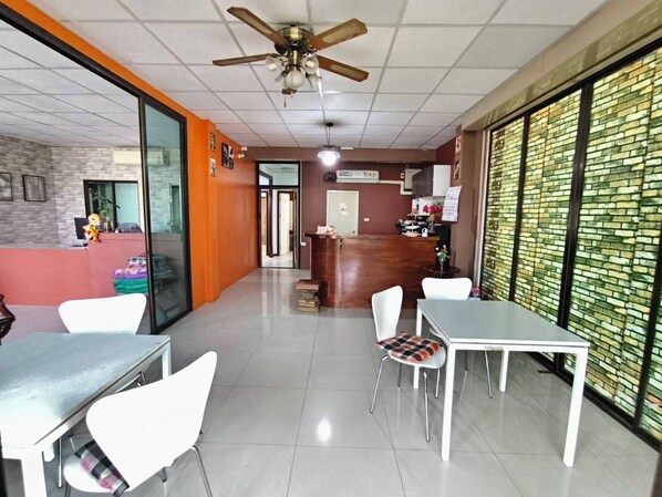 A modern dining area with a reception desk, white chairs, and a ceiling fan.