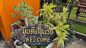 A welcome sign with Thai script, surrounded by potted plants and a concrete planter. - TC House And Cafe (Chiang Mai)