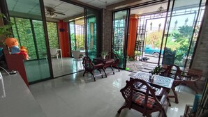 A spacious indoor area with a dining table and chairs, large sliding glass doors leading to a garden, and a ceiling fan. - TC House And Cafe (Chiang Mai)