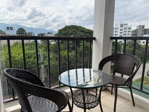 A balcony with two wicker chairs and a glass table, overlooking a cityscape with buildings and greenery. - TC House And Cafe (Chiang Mai)