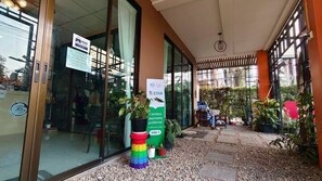A hotel entrance with a glass door, a sign indicating a cashless payment option, and a small outdoor seating area with plants. - TC House And Cafe (Chiang Mai)