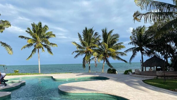 Une piscine à l’eau cristalline, entourée de palmiers et offrant une vue sur l’océan.