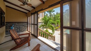 Un balcon avec une chaise en bois, une table et une vue sur un jardin planté de palmiers.