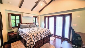 Une chambre à coucher avec un grand lit, un plancher en bois, un ventilateur de plafond et une fenêtre avec des rideaux.
