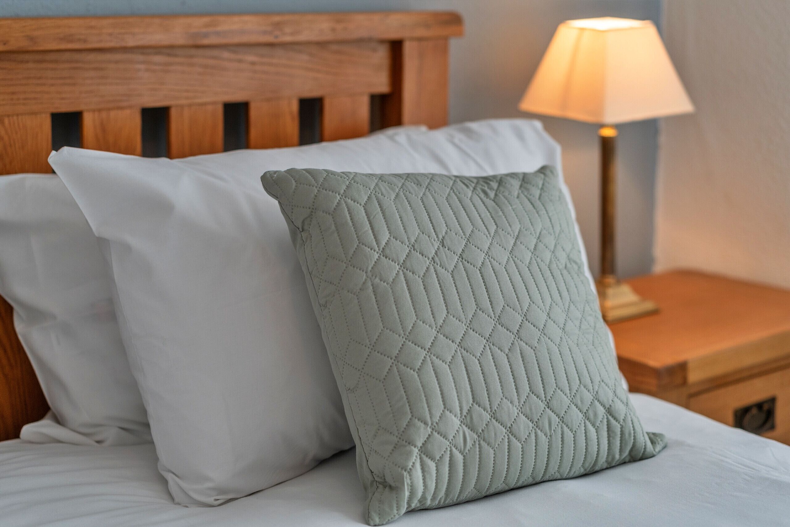 Un lit avec deux oreillers, un blanc et l’autre matelassé, de couleur vert clair.