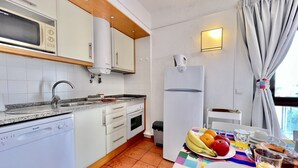 Et kompakt køkken med hvide hårde hvidevarer, en vask og et spiseområde med et bord dækket til morgenmad.