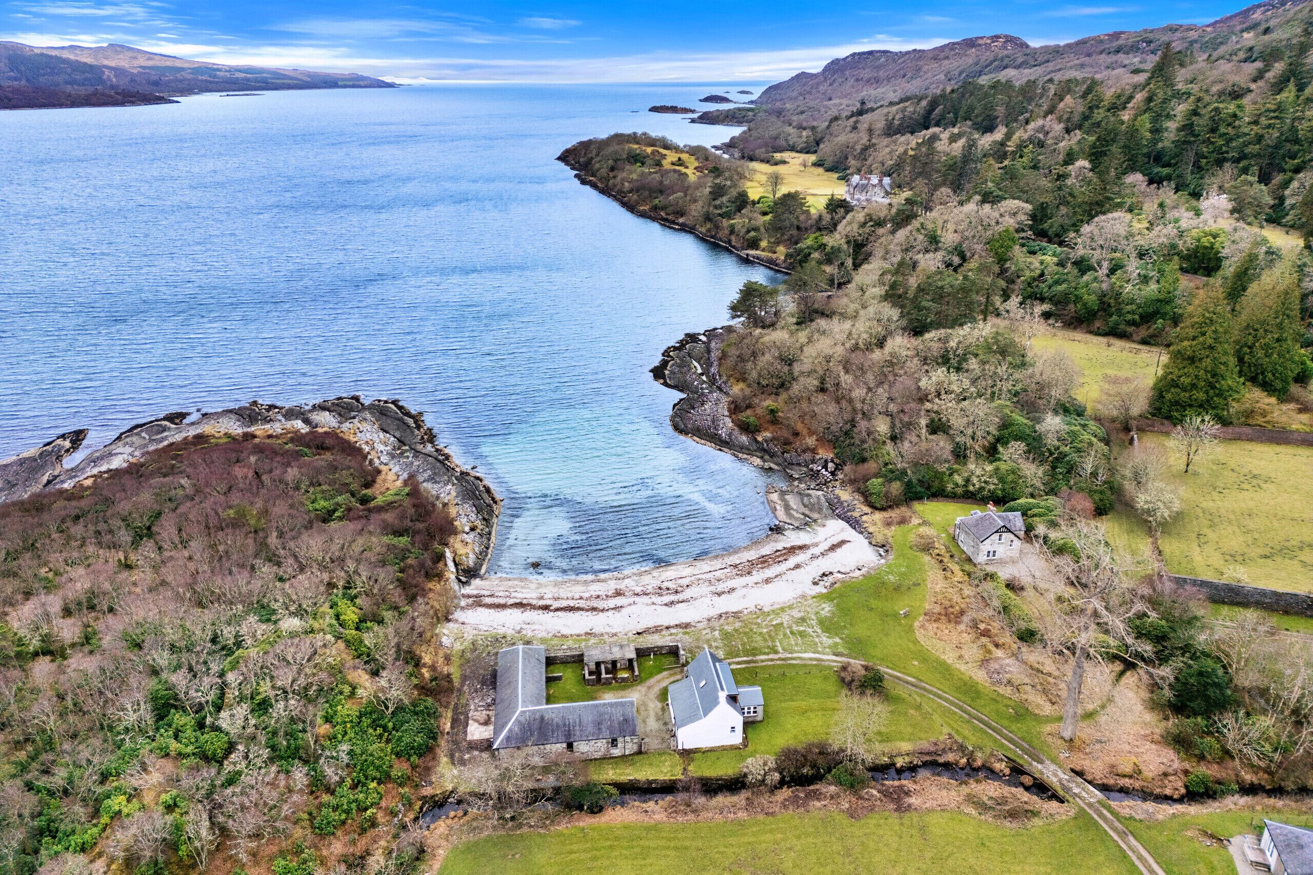 An aerial view of a coastal property with a house, a small dock, and surrounding greenery.