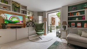 A modern living room with a flat-screen TV, a green chair, a sofa, and a dining area with chairs and a table.