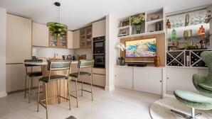 A modern kitchen with a dining area, featuring a TV, bar area, and a unique green chandelier.